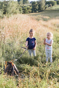 Smiling girl preparing marshmallow on campfire by sister standing on grassy field