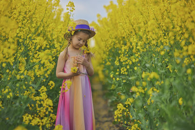 Young woman standing amidst yellow flowering plants on field