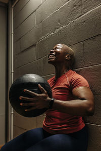 Determined female athlete doing wall sit exercise with medicine ball at gym