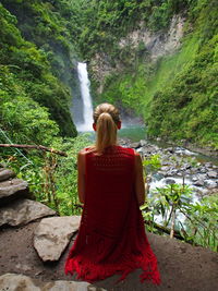 Rear view of woman against waterfall at forest