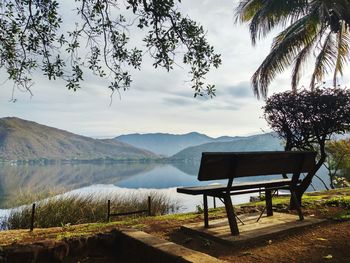 Bench by lake against sky