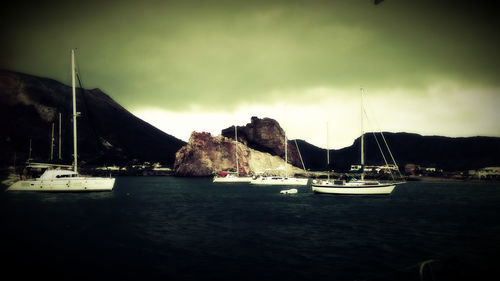 Boats moored in sea against cloudy sky