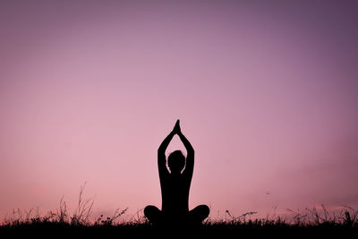 Silhouette woman practicing yoga on field against sky during sunset