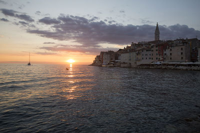 Sea by buildings against sky during sunset