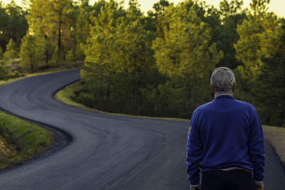 Rear view of man standing on road amidst trees