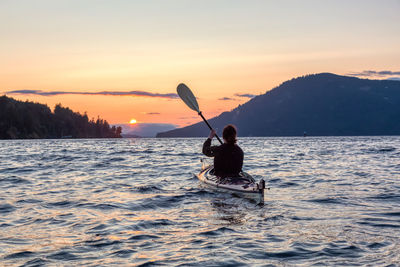 Man on boat in sea against sky during sunset