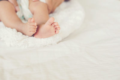 Cropped hands of mother holding baby feet on bed