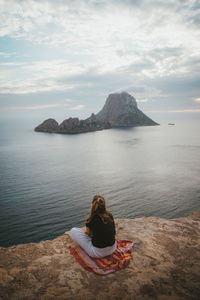 Rear view of woman sitting on rock against sea and sky