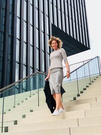 Full length portrait of smiling businesswoman walking down on steps in city