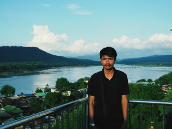 Portrait of smiling man standing by railing against sky