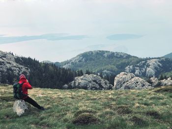 Rear view of man sitting on rock at mountain 