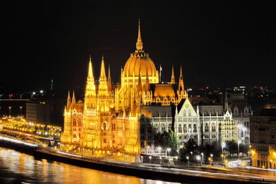 Illuminated hungarian parliament building by danube river against sky