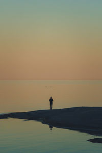 Rear view of man walking at beach against sky during sunset