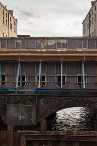 Bridge over river by buildings against sky