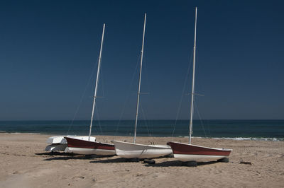 Sailboats moored on beach against clear sky