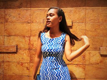 Young woman looking away while standing against wall