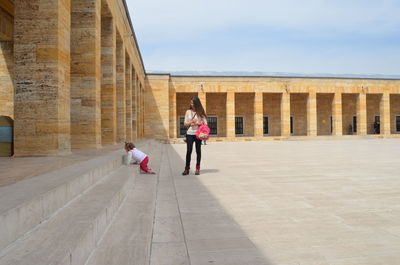 Women walking on walkway by building against sky