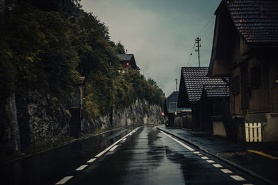 Empty road amidst buildings against sky during rainy season