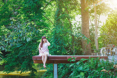 Young woman sitting by plants against trees