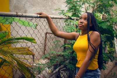 Side view of woman standing by fence against plants