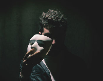 Portrait of man holding mask over black background
