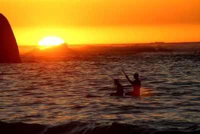 Silhouette man in sea against sky during sunset