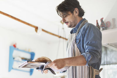 Side view of man holding freshly baked bread in tray at home