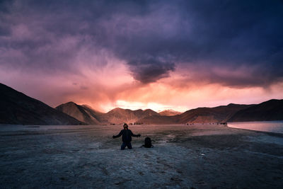 Man kneeling on land against cloudy sky at sunset