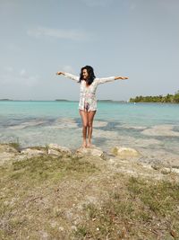 Full length of young woman with arms raised on beach