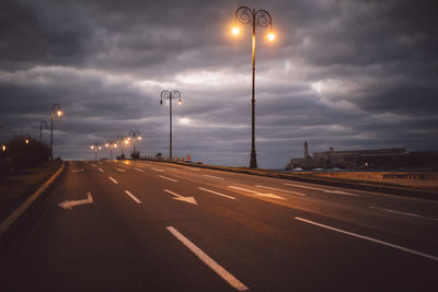 Street lights on road against cloudy sky