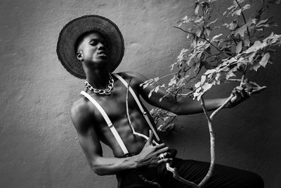 Young man holding plant while standing against wall