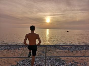 Rear view of shirtless man looking at sea against sky during sunset