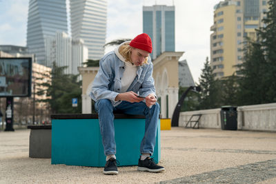 Side view of young man sitting on street in city