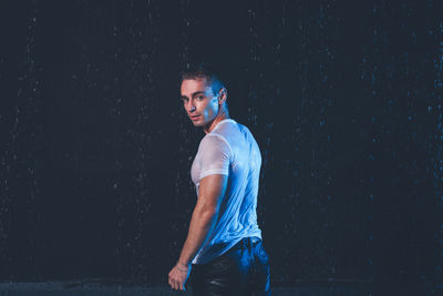 Portrait of young man standing against black background