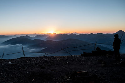 Silhouette man standing on mountain against sky during sunset