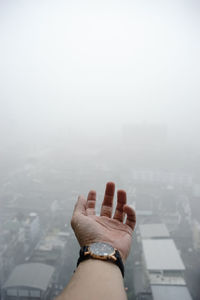 Cropped image of man hand against cityscape during foggy weather