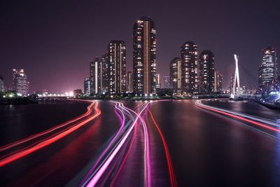 Light trails on street against illuminated city buildings at night