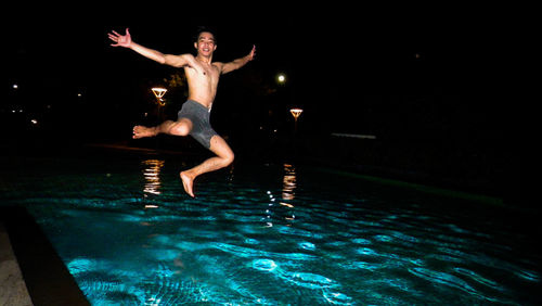Portrait of shirtless man jumping in swimming pool at night