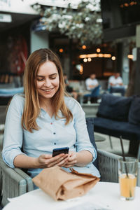 Young woman using mobile phone while sitting on table