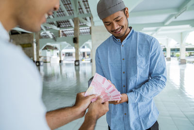 Smiling man giving money to friend at mosque