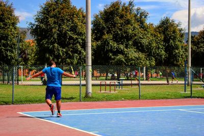 Rear view full length of man playing tennis at court on sunny day