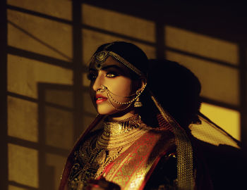 Bride wearing sari and jewelries standing against wall