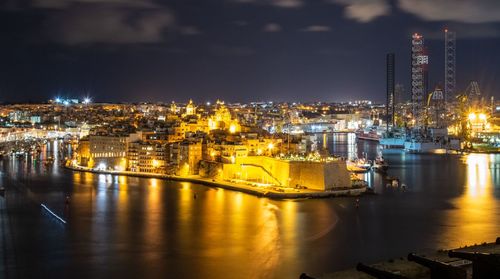 Illuminated city by river against sky at night