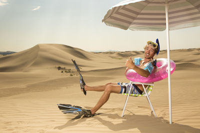 Young man sitting on sand at beach against clear sky