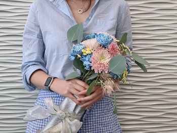 Midsection of woman holding bouquet against wall