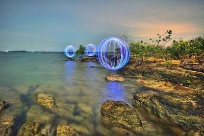 Ferris wheel on rocks by lake against sky