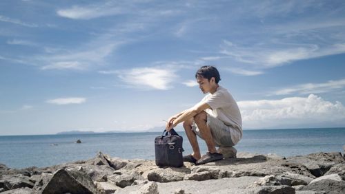 Woman sitting on rock at beach against sky