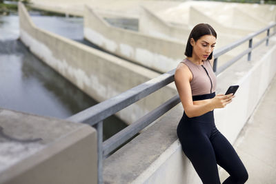 Young woman using mobile phone while standing on bridge