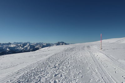 Snow covered landscape against clear blue sky