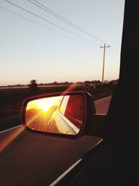Car on side-view mirror against sky during sunset